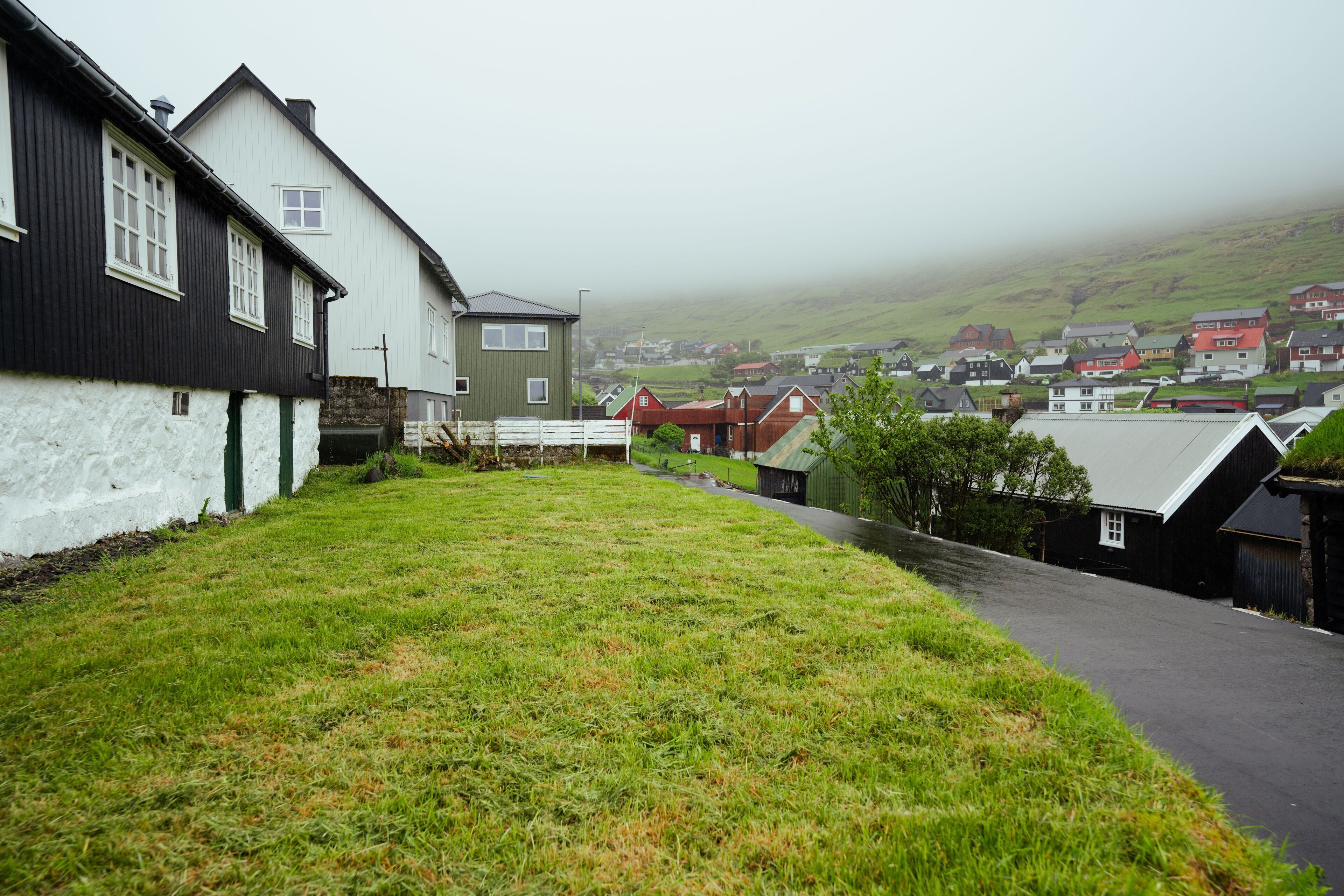 Une rue de campagne bordée de maisons, avec un espace verdoyant et un arrière-plan brumeux.