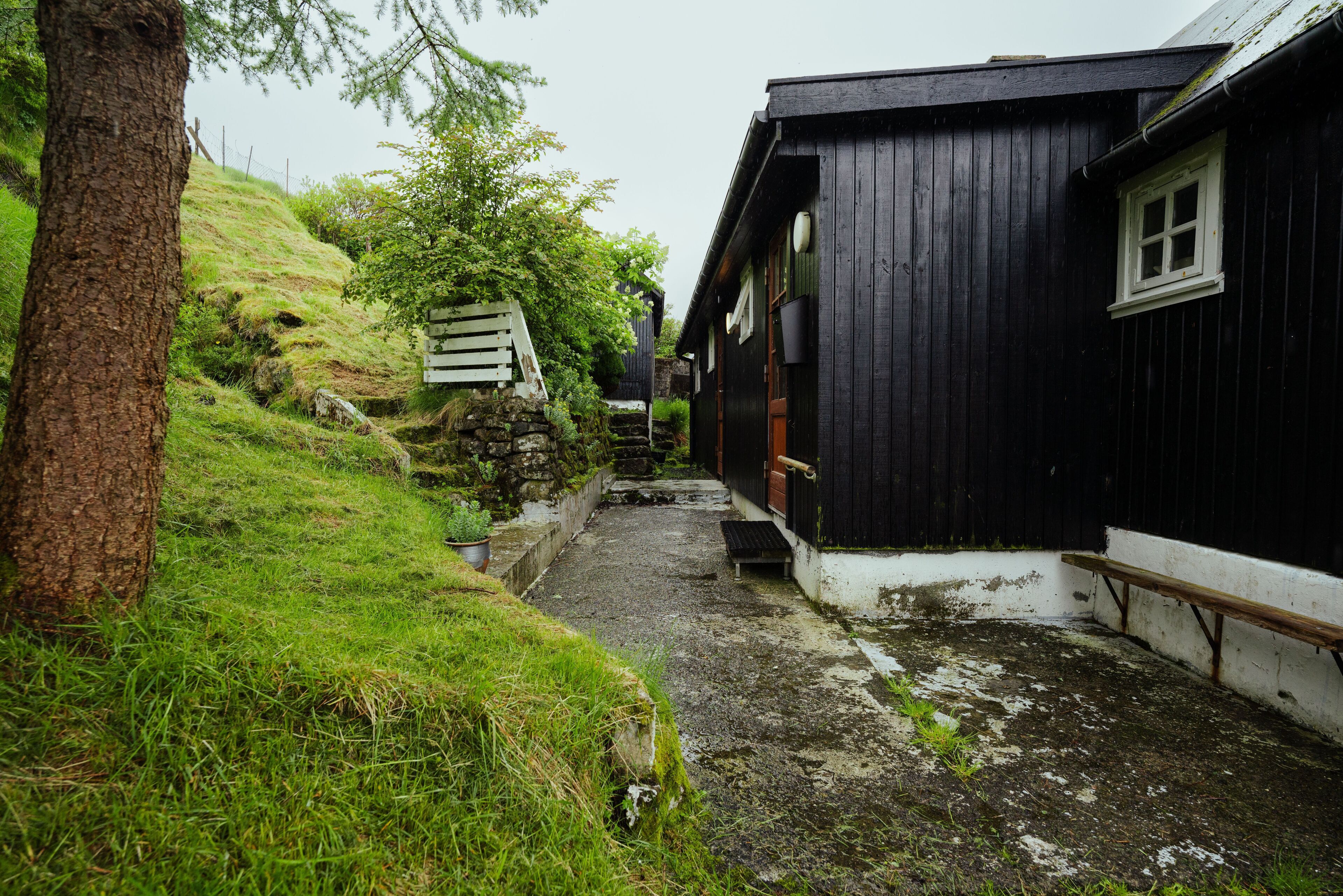 A narrow pathway leading to a wooden building with a white window and a wooden bench.
