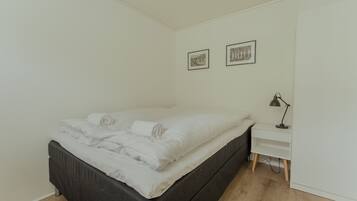 A bedroom with a bed, a bedside table with a lamp, and two framed pictures on the wall.