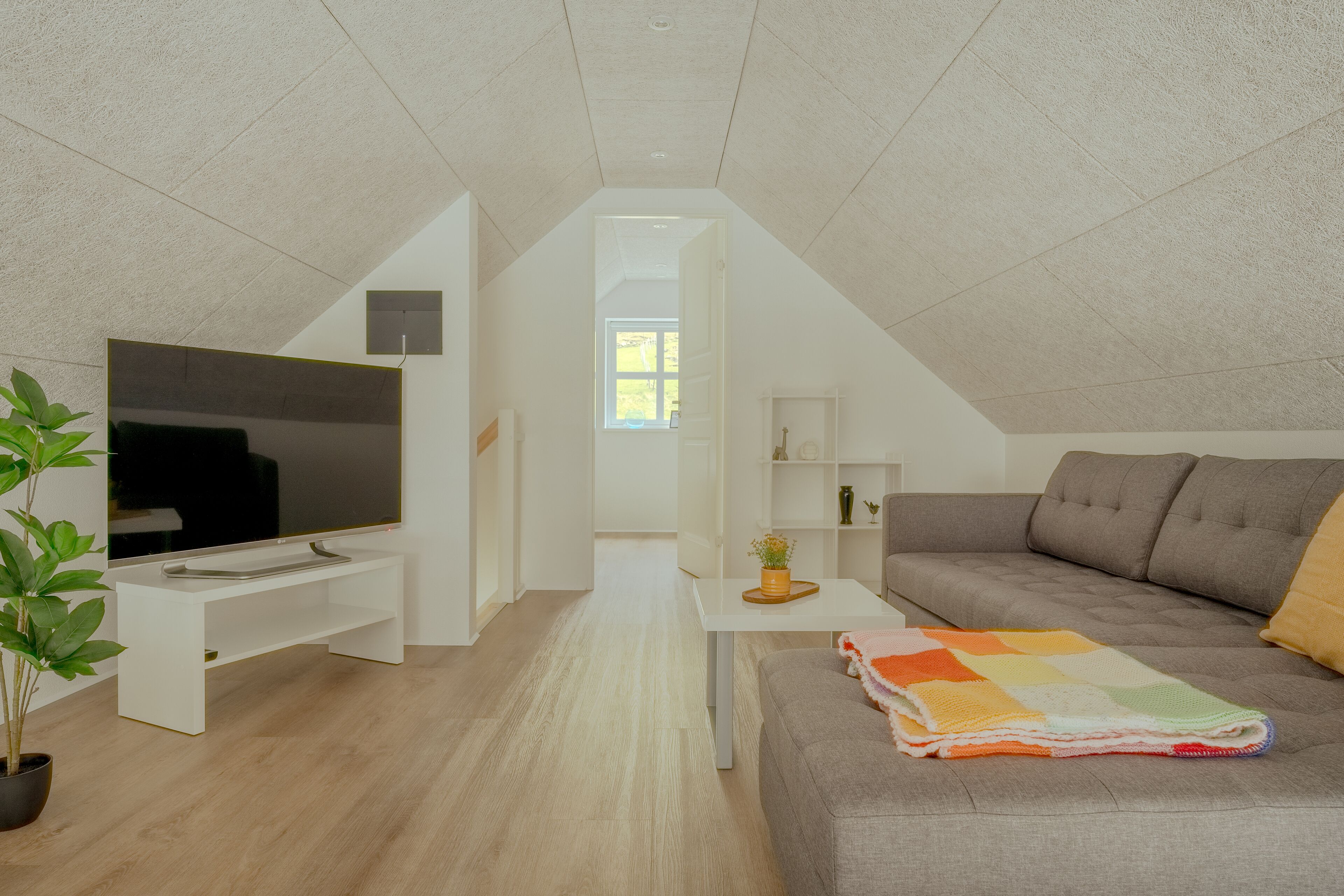 Ein modernes Wohnzimmer mit Flachbildfernseher, einem grauen Sofa, einem weißen Couchtisch und einer Topfpflanze.