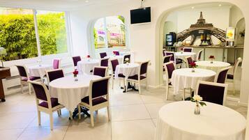 A restaurant with round tables and purple chairs, large windows with greenery outside, and a decorative archway with a model of the Eiffel Tower.