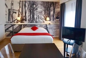Una habitación de hotel con cama, televisión, escritorio y un mural en la pared.