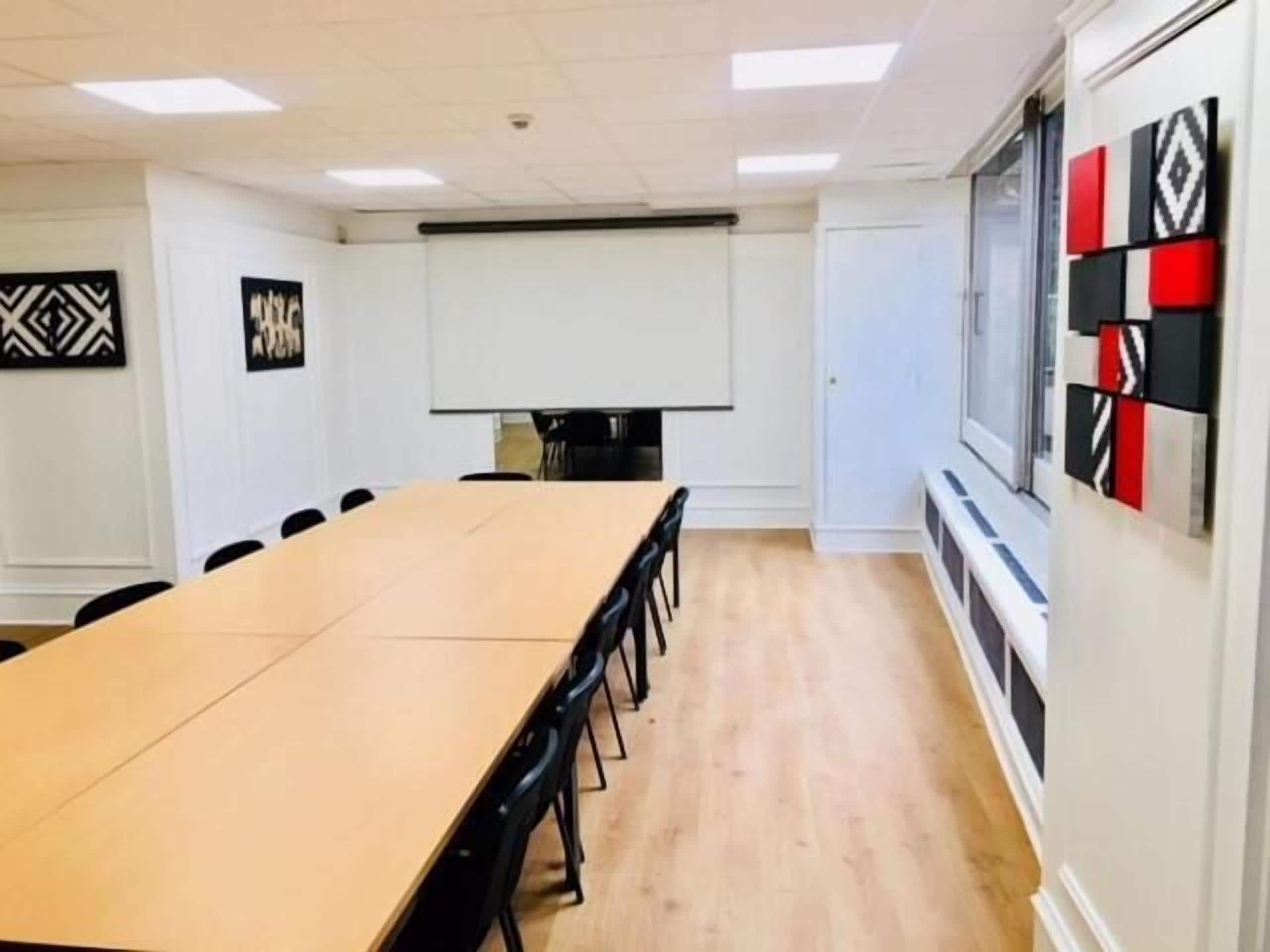 A conference room with a long table, black chairs, a projector screen, and decorative wall panels.