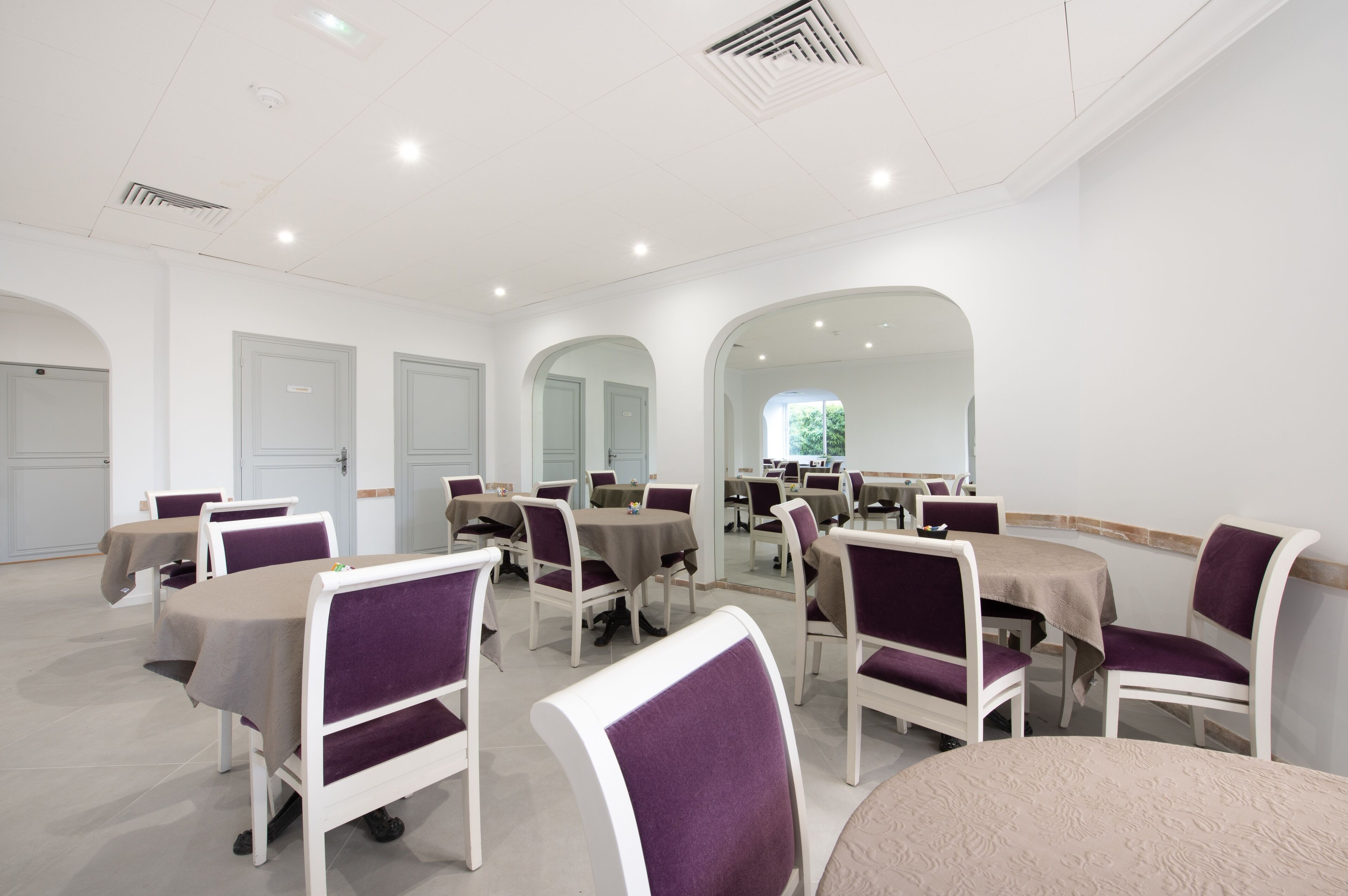 A conference room with white walls, multiple tables, and purple chairs.