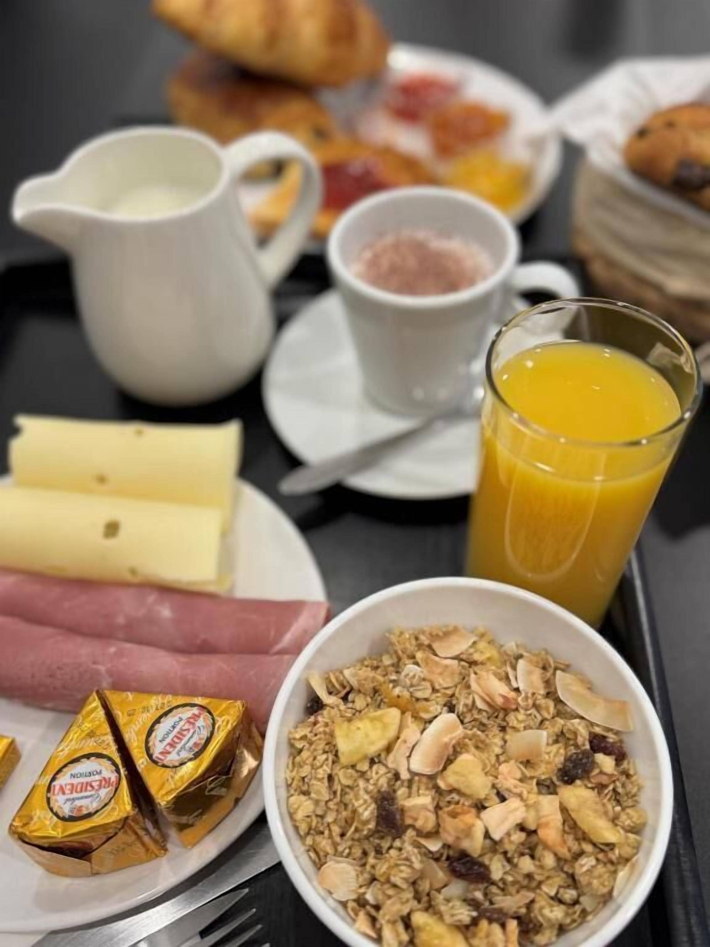 A breakfast table with various food items including cheese, ham, granola, and a glass of orange juice.
