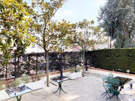 Un patio al aire libre con una mesa y sillas, rodeado de árboles y un seto.