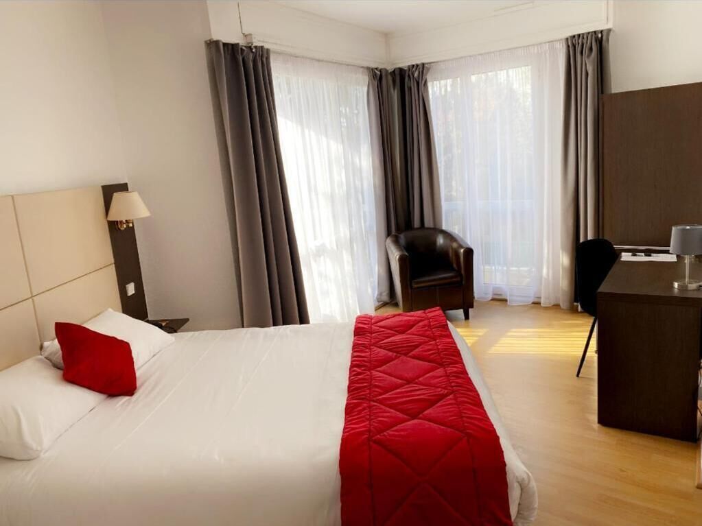 A hotel room with a bed, a desk, a chair, and a lamp.