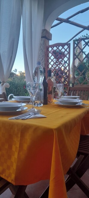 An outdoor dining area with a table set for two, featuring a yellow tablecloth, clear glassware, and a bottle. - Apartment I Gelsomini ## (Tanaunella)