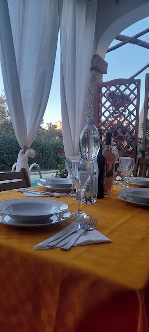 An outdoor dining area with a table set for two, featuring a clear glass bottle, plates, cutlery, and a napkin. - Apartment I Gelsomini ## (Tanaunella)