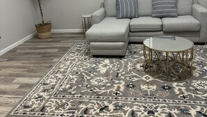 Un salon avec un canapé gris, une table basse ronde, un tapis à motifs et une plante en pot.