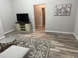 A living room with a TV on a wooden stand, a patterned rug, and a small round table.