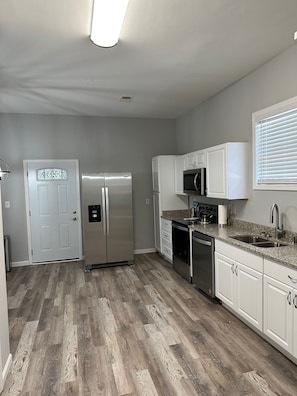 A modern kitchen with white cabinets, stainless steel appliances, and a herringbone wood floor.