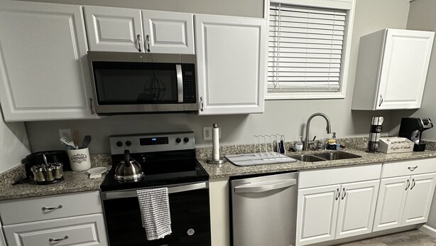 Une cuisine moderne avec des armoires blanches, des appareils en acier inoxydable, un comptoir en granit et un plancher en bois disposé en motif chevron.