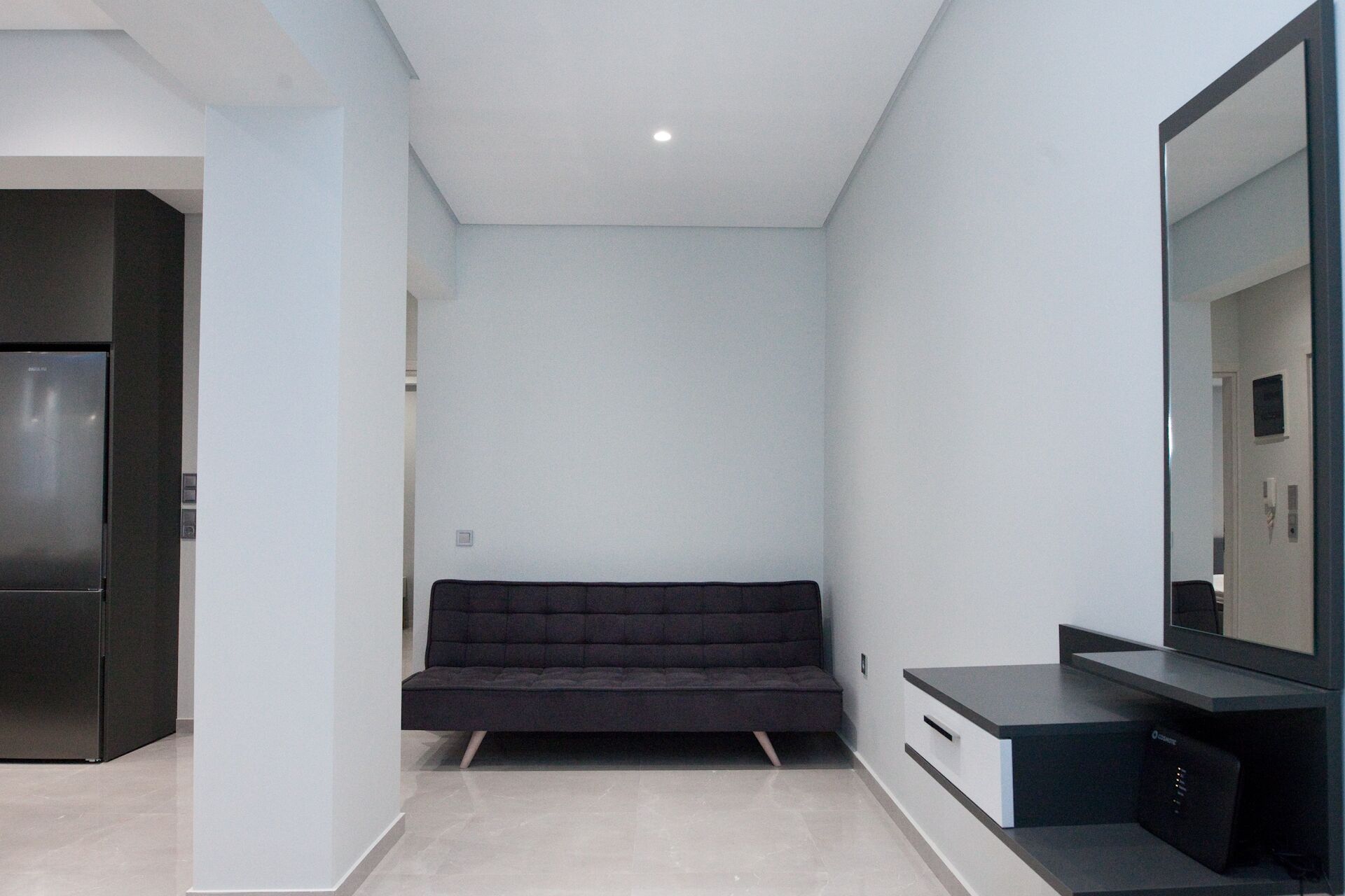 A modern, minimalist room with a dark sofa, a built-in TV, and a large mirror.