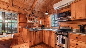 A wooden cabin kitchen with a stove, oven, microwave, and wooden cabinets. - Cozy Cabin w/ Hot Tub & Fenced in Yard for Pets (Hot Springs)