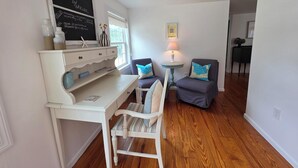 Un salon chaleureux avec un bureau blanc, deux chaises, une petite table ronde avec une lampe et une bibliothèque.