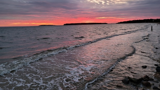 Une plage avec des vagues et un coucher de soleil.