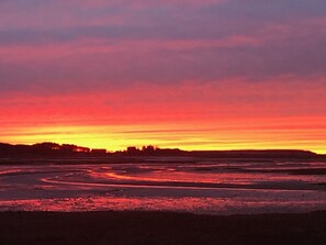 Ein Sonnenuntergang über einer flachen Landschaft, im Vordergrund fließt ein Fluss oder See.