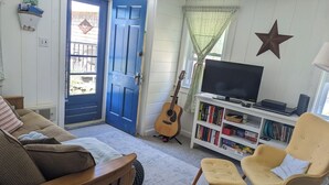 Una sala de estar acogedora con una puerta azul, una guitarra, una estantería y un televisor.