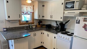 Una cocina compacta con alacenas blancas, una encimera de granito, estufa, microondas y refrigerador.