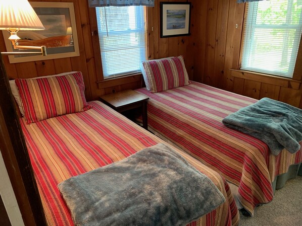 A cozy room with two beds, a small table, and a lamp. - Sweet Cape Cod Cottage! (CS0011) (Wellfleet)