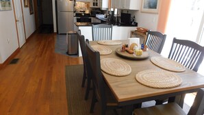 A modern kitchen with wooden flooring, a dining table set with placemats, and a refrigerator. - Immaculate Home in the Woods (CS0033) (Wellfleet)