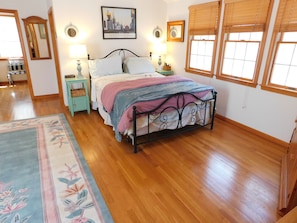 Une chambre à coucher comprenant un lit, deux tables de chevet, une commode, un miroir et une fenêtre avec des stores.