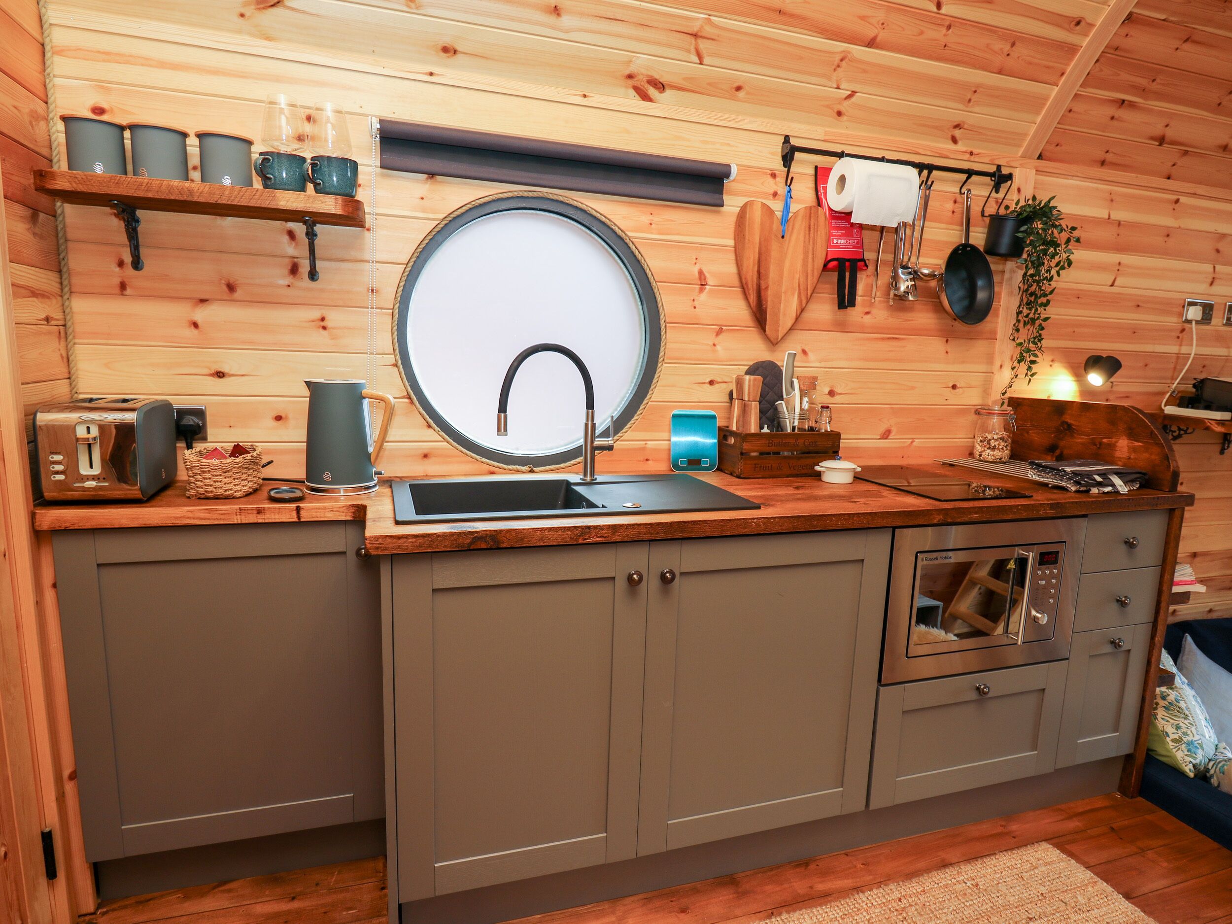 Una cocina compacta con un espejo redondo sobre el lavabo, una tostadora, un hervidor y un horno pequeño.