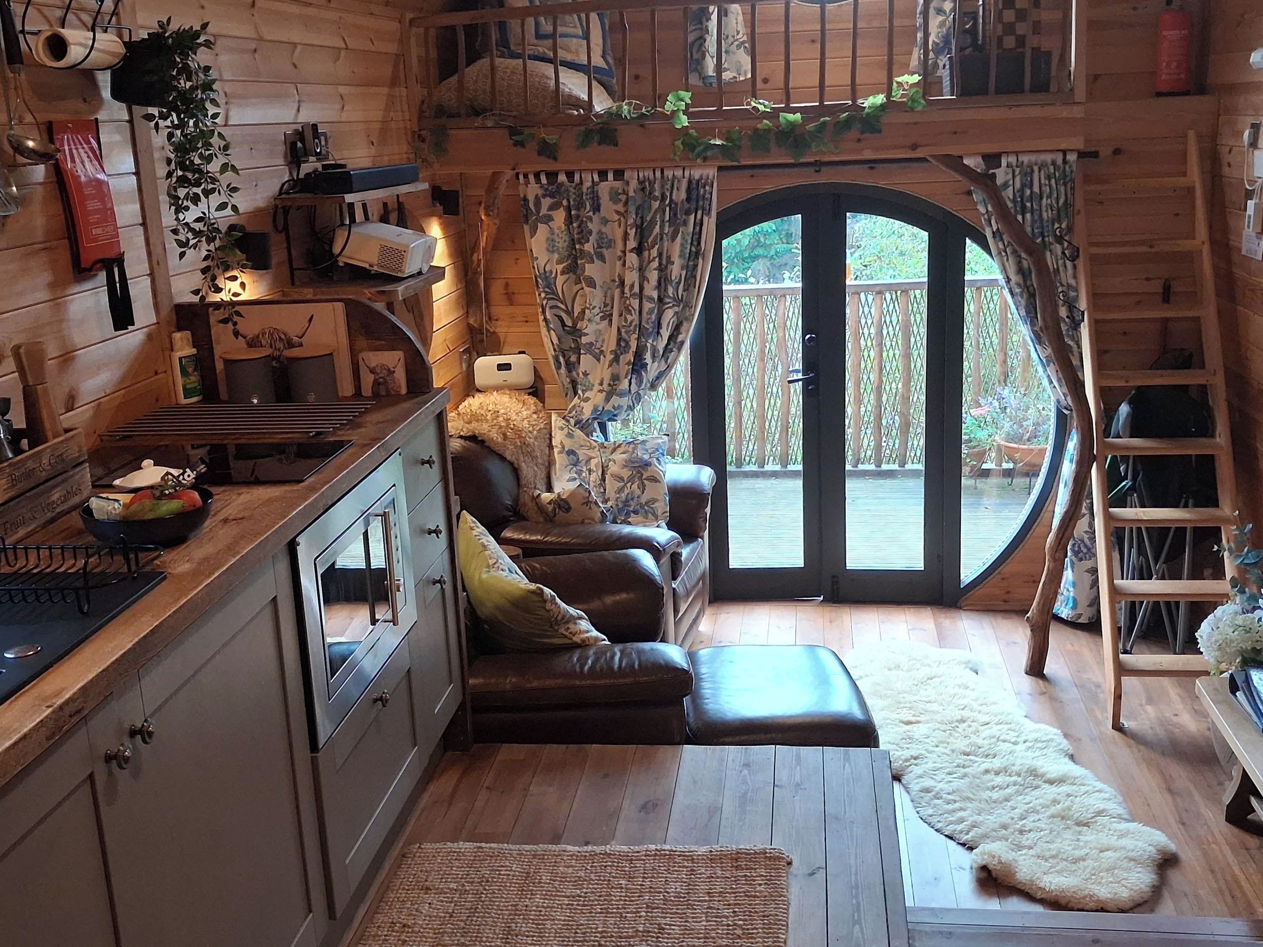 A cozy cabin interior with a wooden interior, a dining area, a sofa, and a large window.