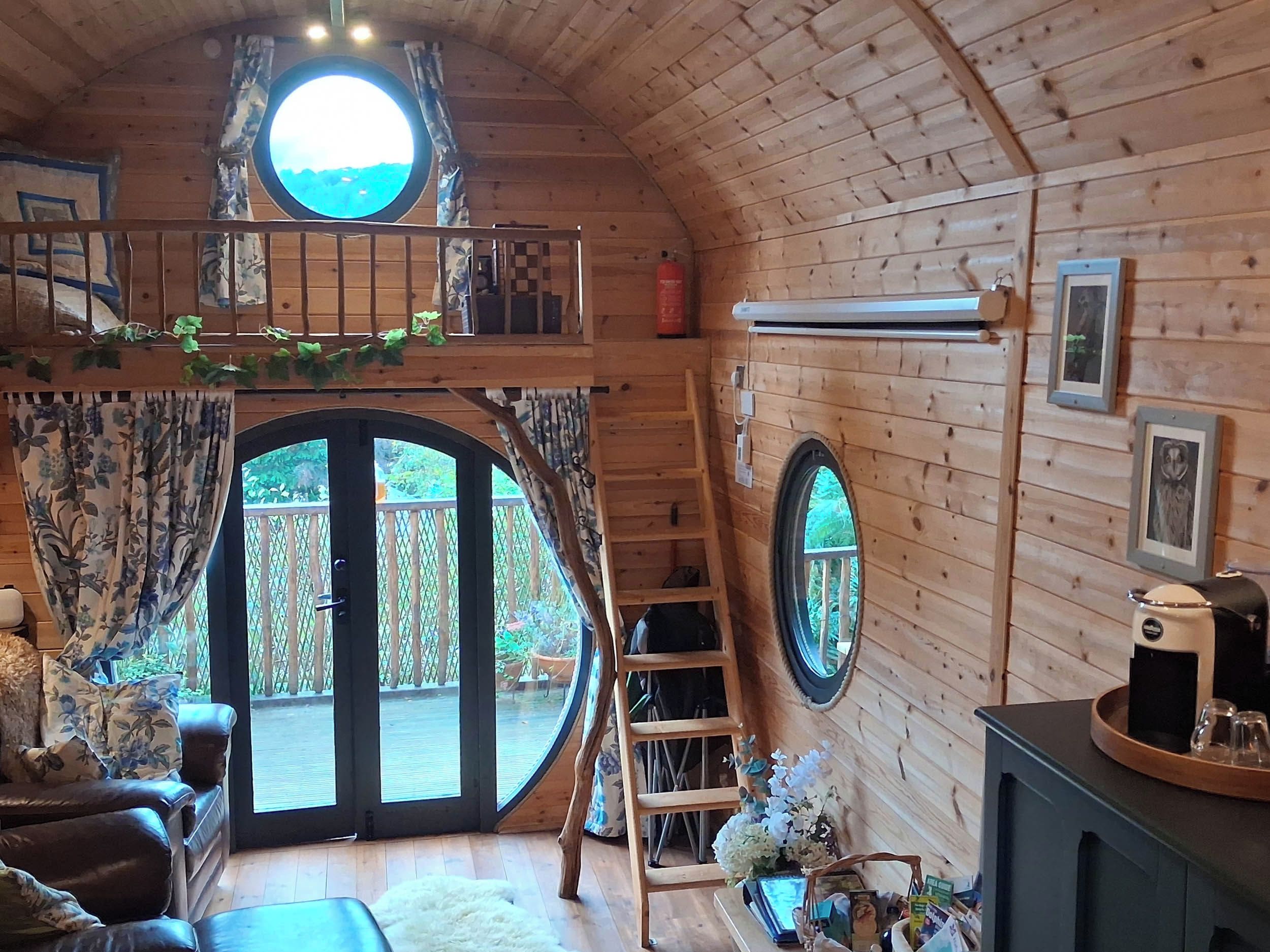 Una cabaña acogedora con un dormitorio en loft, un comedor y un amplio ventanal con vistas a una terraza de madera.