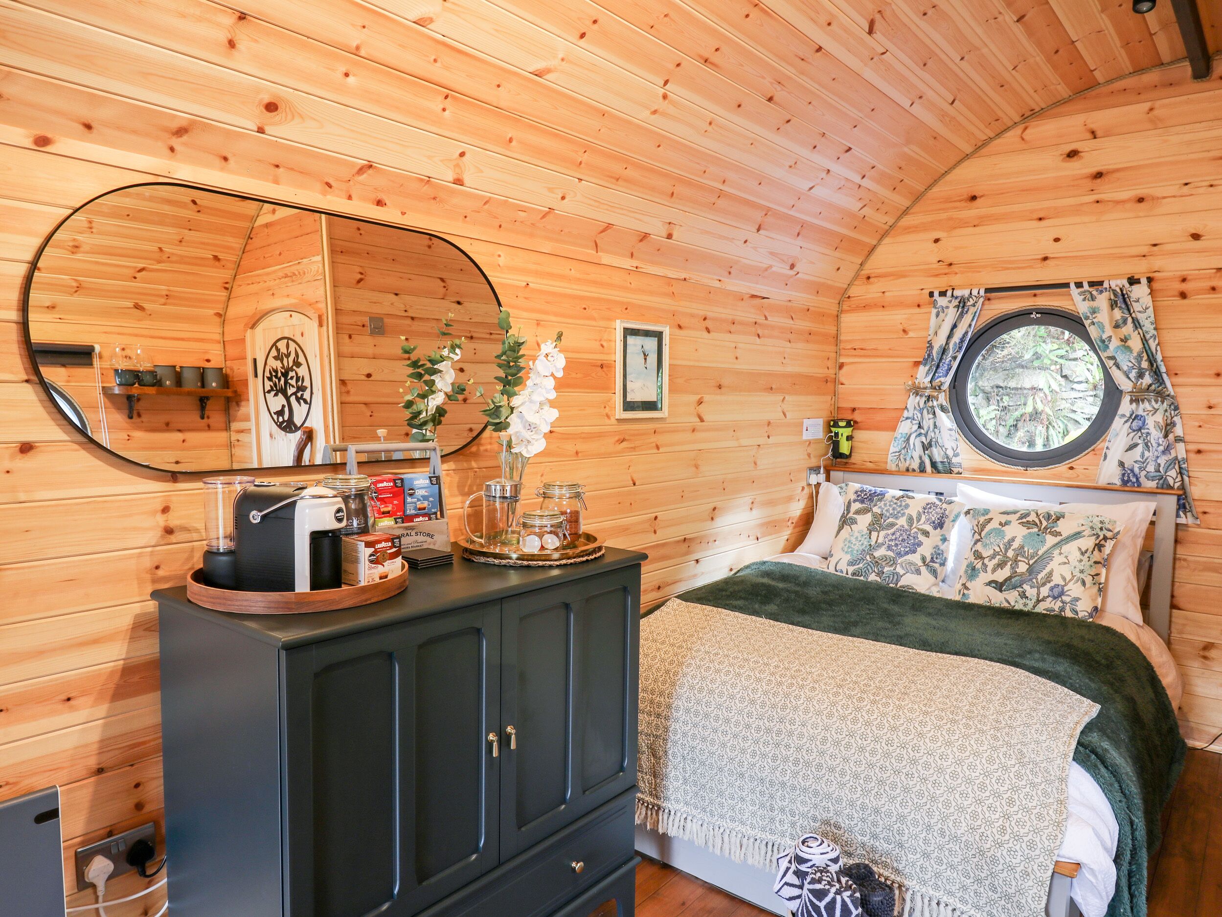 Une chambre confortable dans un chalet en bois, avec un lit, une commode contenant des articles de toilette, un miroir et une fenêtre avec des rideaux.