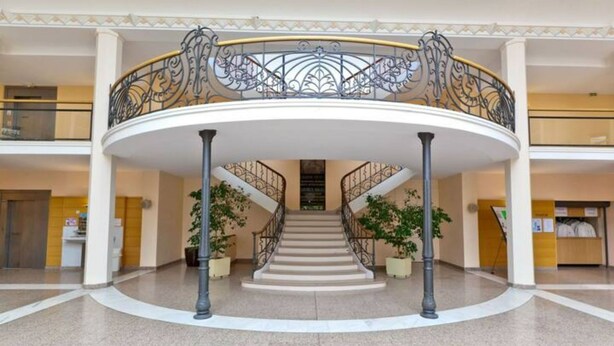 A spacious atrium with a central staircase, columns, and decorative railings. - Vittel Loc's : Le 214 Classé 3 Osez L'expérience! (Vittel)
