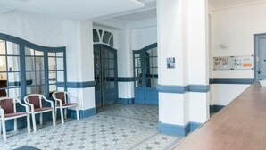 A reception area with a check-in counter, a seating area with chairs, and a patterned floor. - Vittel Loc's : Le 214 Classé 3 Osez L'expérience! (Vittel)