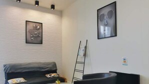 A modern living room with a black sofa, a glass coffee table, and two black chairs. There is a framed picture on the wall and a blackboard leaning against the wall. - Vittel Loc's : Le 214 Classé 3 Osez L'expérience! (Vittel)