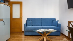 A room with a blue sofa, a glass coffee table, a wooden door, and a white cabinet. - Domus Alberico 11 (Vaticano) (Roma)