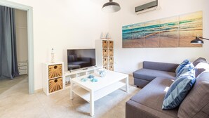 Uma sala de estar moderna com televisão de tela plana, mesa de centro branca, sofá cinza e uma grande pintura abstrata na parede.