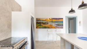 Uma cozinha moderna com fogão, cadeiras brancas e uma pintura grande na parede.