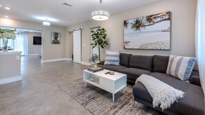 Un salon spacieux avec un canapé gris, une table basse blanche et un grand tableau représentant une scène de plage.