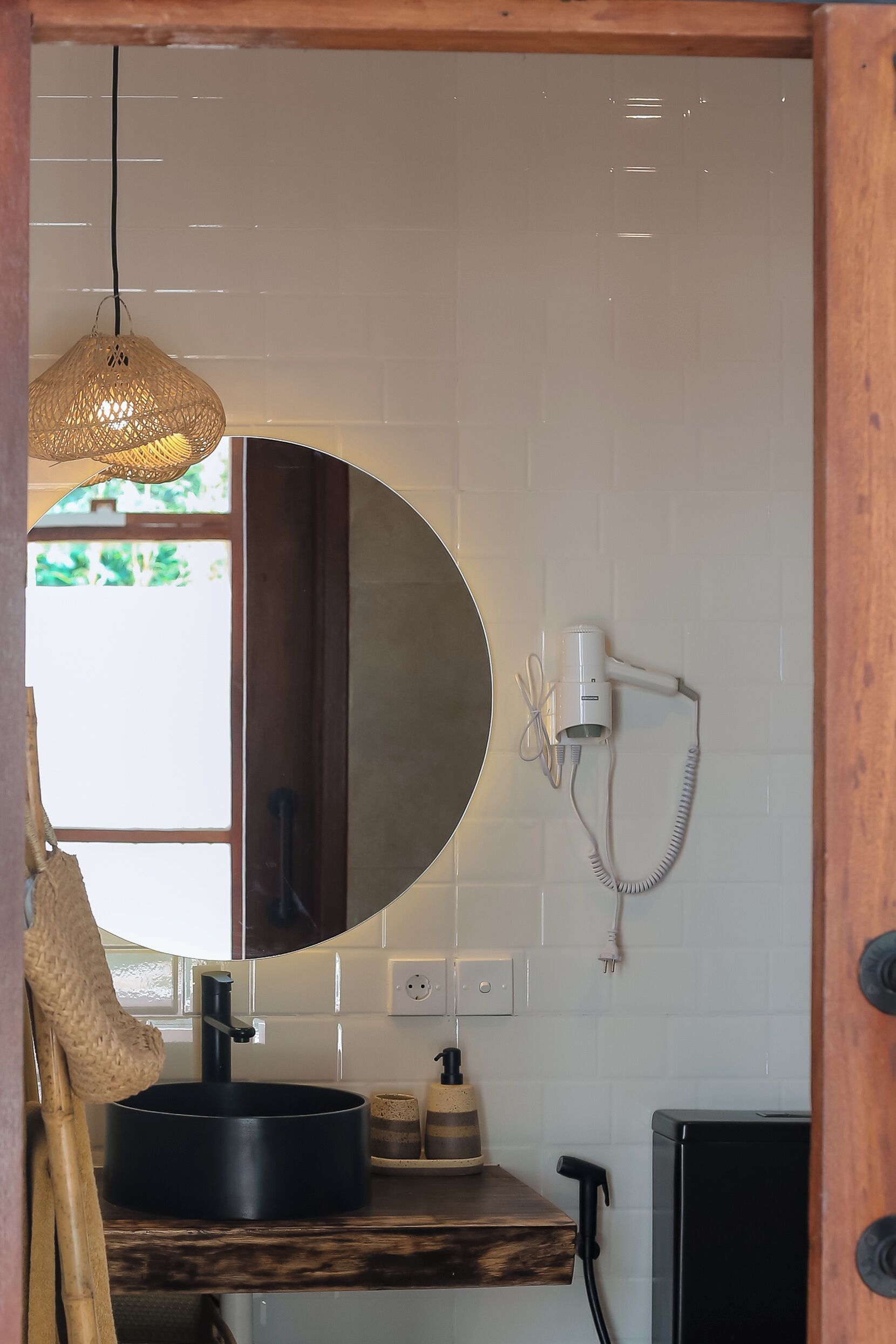 Un baño con un espejo redondo, un secador de pelo, un lavabo y un estante de madera.