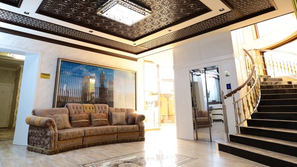A spacious lobby with a large, plush sofa, a grand staircase, and a decorative ceiling. - Saroy Palace Hotel (Qarshi)