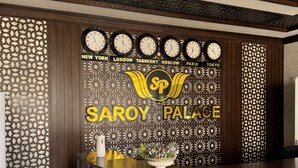 A reception desk with a decorative wall featuring clocks and city names. - Saroy Palace Hotel (Qarshi)