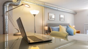 A modern bedroom with a glass desk, a laptop, a bedside lamp, a bed with colorful pillows, and a headboard. - Studio degli Artisti by Wonderful Italy (Torino)