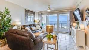 A living room with a leather sofa, a table with a lamp, a large mirror, and a view of the ocean through a sliding glass door. - Regency Isle 303 by Liquid Life (Orange Beach)
