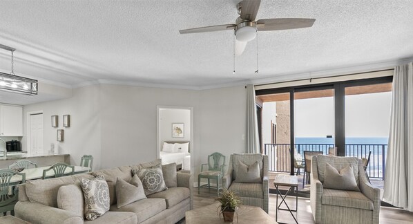 A spacious living area with a balcony overlooking the sea, a ceiling fan, and a kitchen area. - Four Seasons 604W by Liquid Life (Orange Beach)