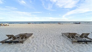 A beach with wooden lounge chairs and a sandy shore. - Island Royale 506 Penthouse by Liquid Life (Gulf Shores)