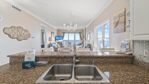 A kitchen with granite countertops, a double sink, and a view to the living area. - Island Royale 506 Penthouse by Liquid Life (Gulf Shores)