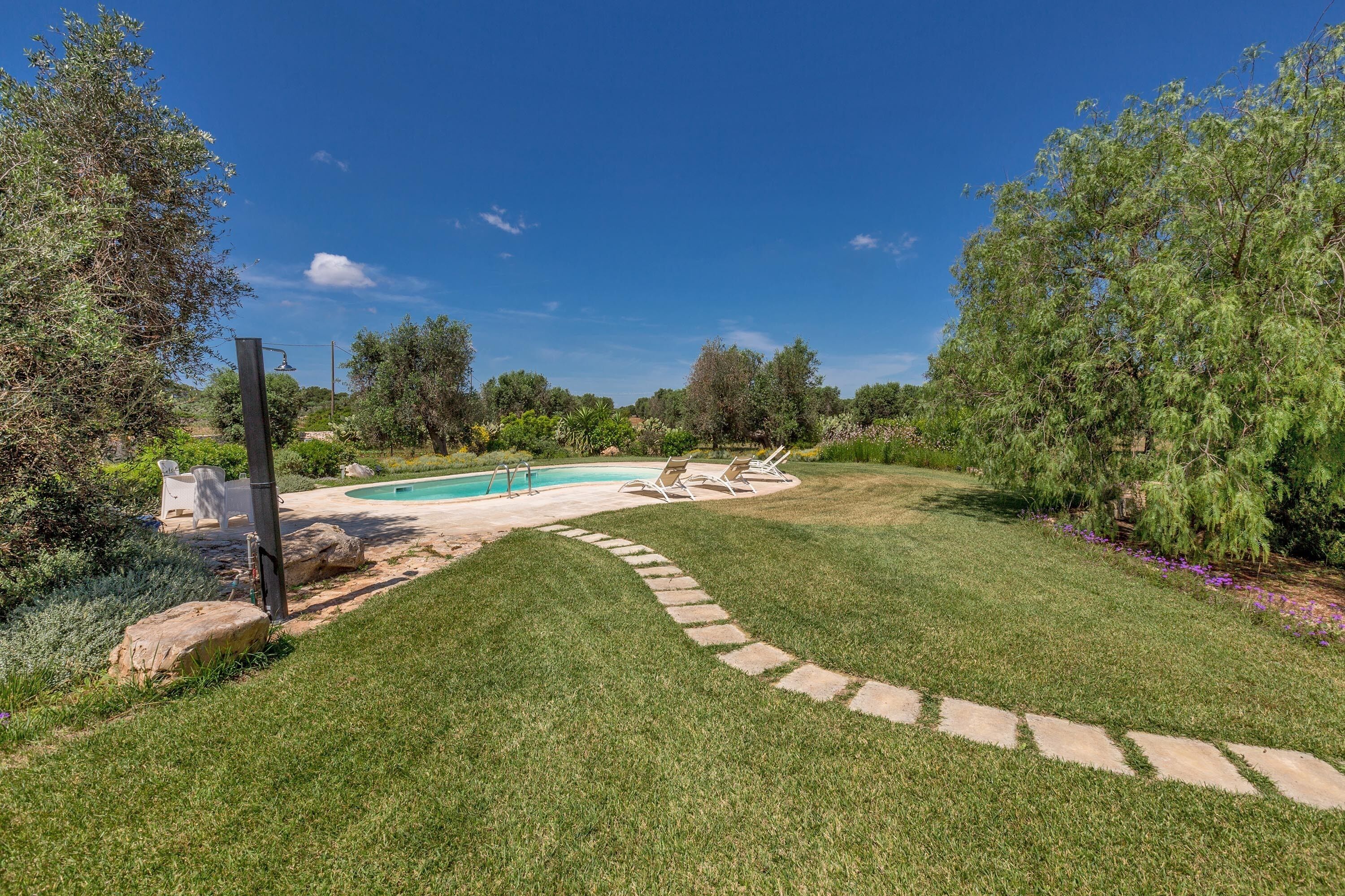 A backyard with a swimming pool, stone pathway, and outdoor furniture.