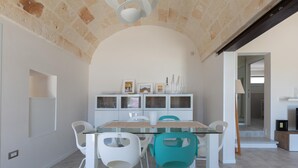 Een eetruimte met een glazen tafel, witte en turquoise stoelen en een plafond van natuursteen.