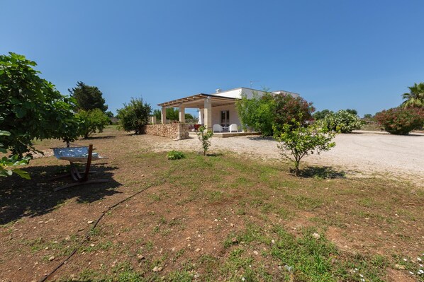 A house with a covered patio, a small garden, and a dirt driveway.