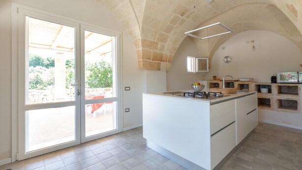 Een ruime keuken met een groot eiland, een plafond met stenen bogen en een uitzicht door de glazen deuren naar buiten.